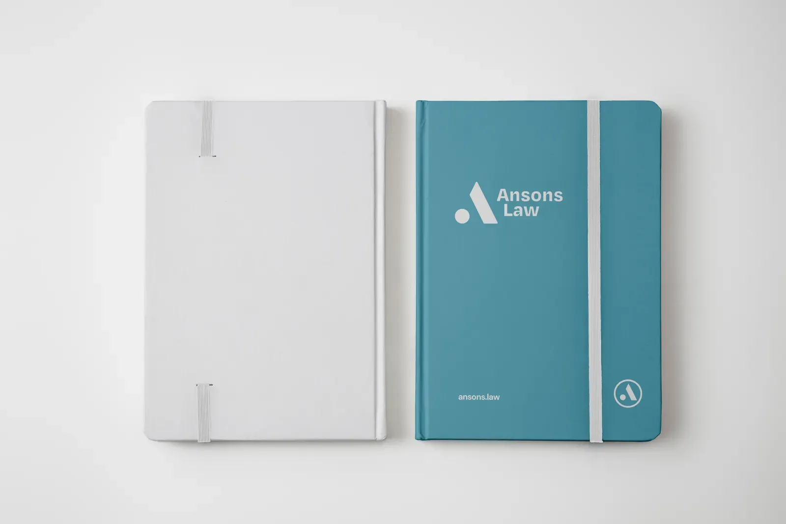 A white notebook and a teal Ansons Law branded notebook side by side on a pale background.