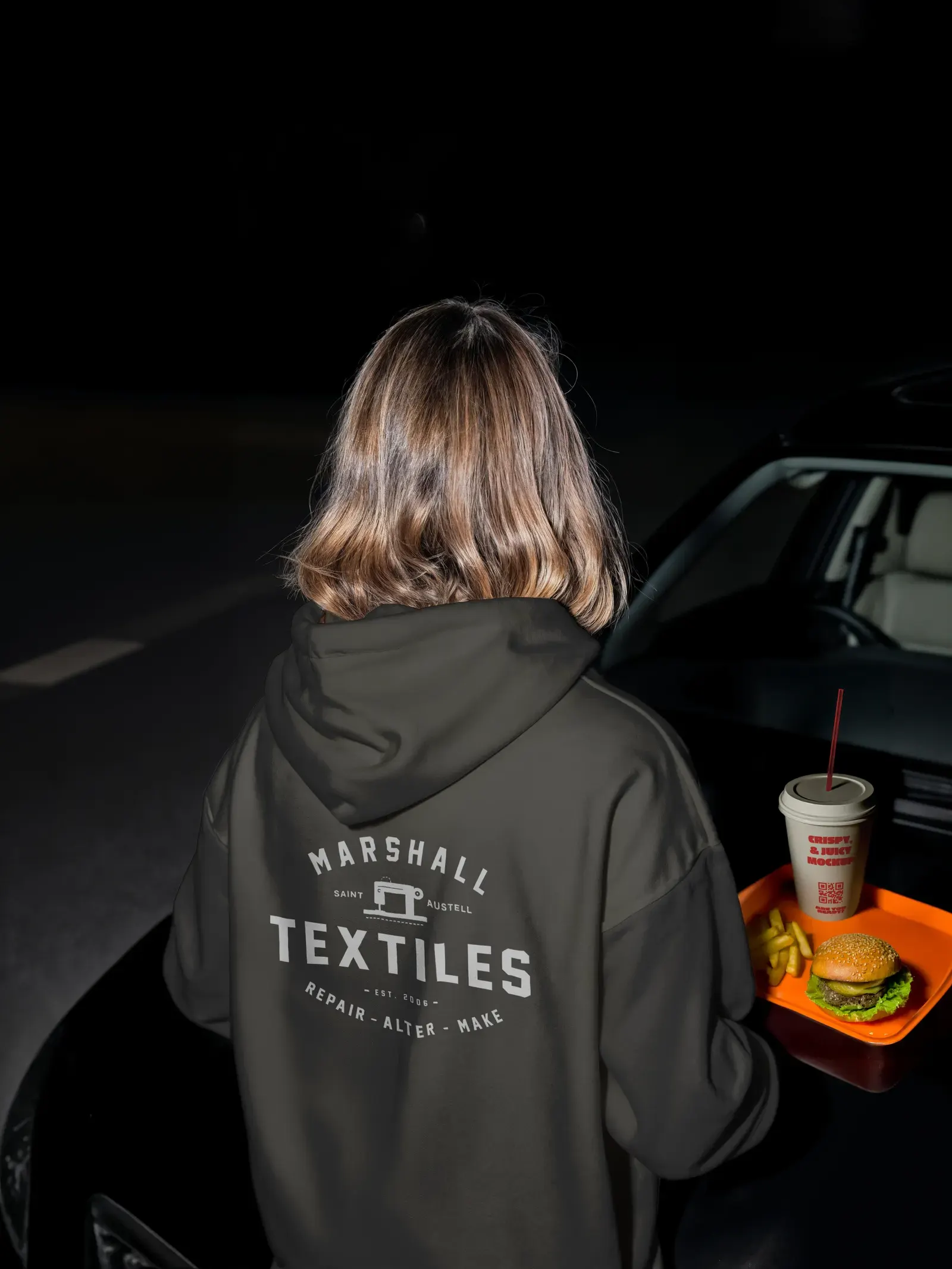 A person seen from behind wearing a dark hoodie with the Marshall Textiles badge on the back.
