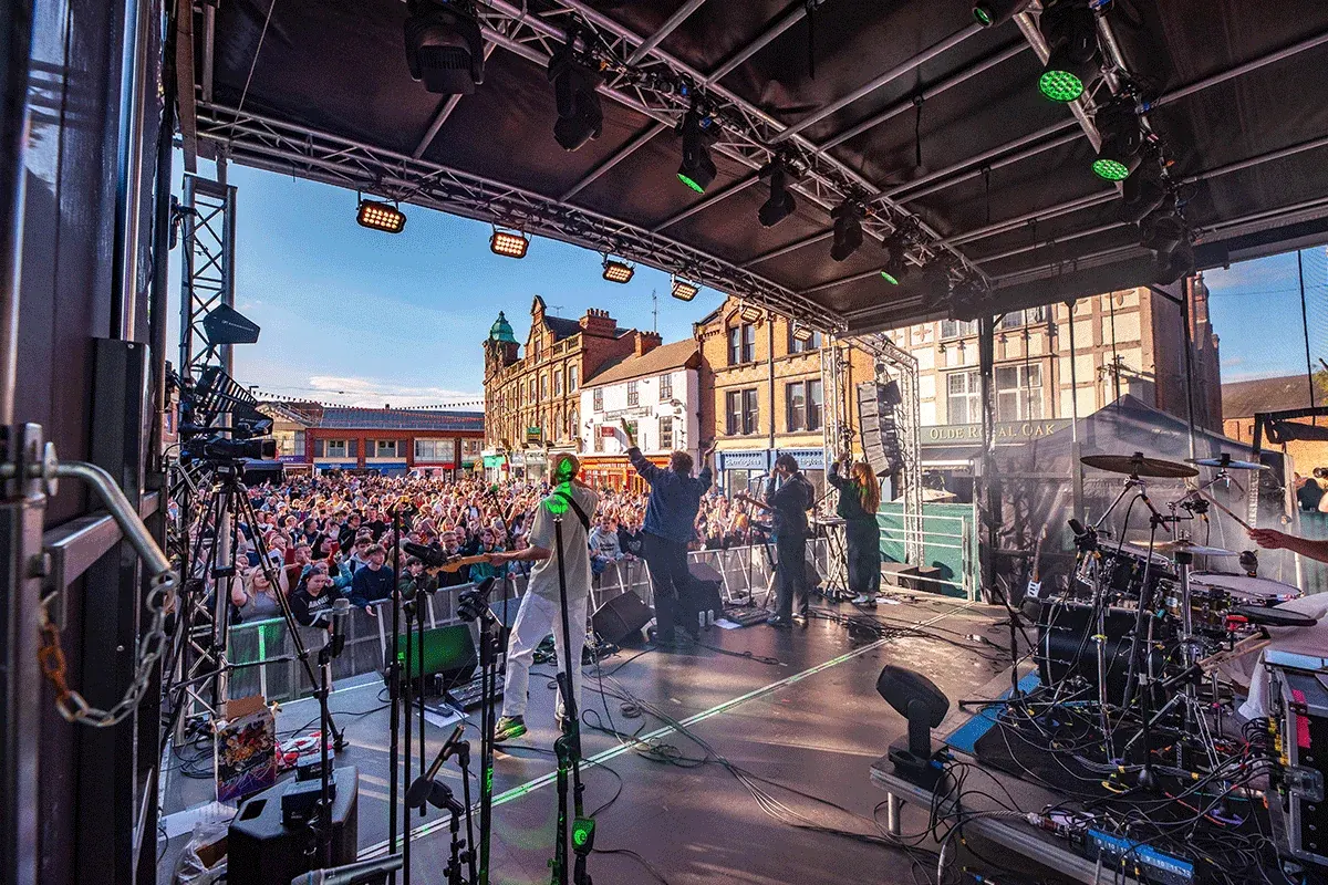 The view from the back of the Sonic Boom main stage, looking past the drum kit and the band to a packed Market Place in Burton upon Trent on a sunny evening.