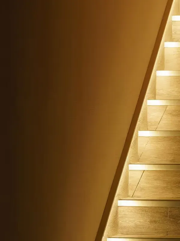 A warm, softly lit staircase rising beside a plain wall, each step edged with light.